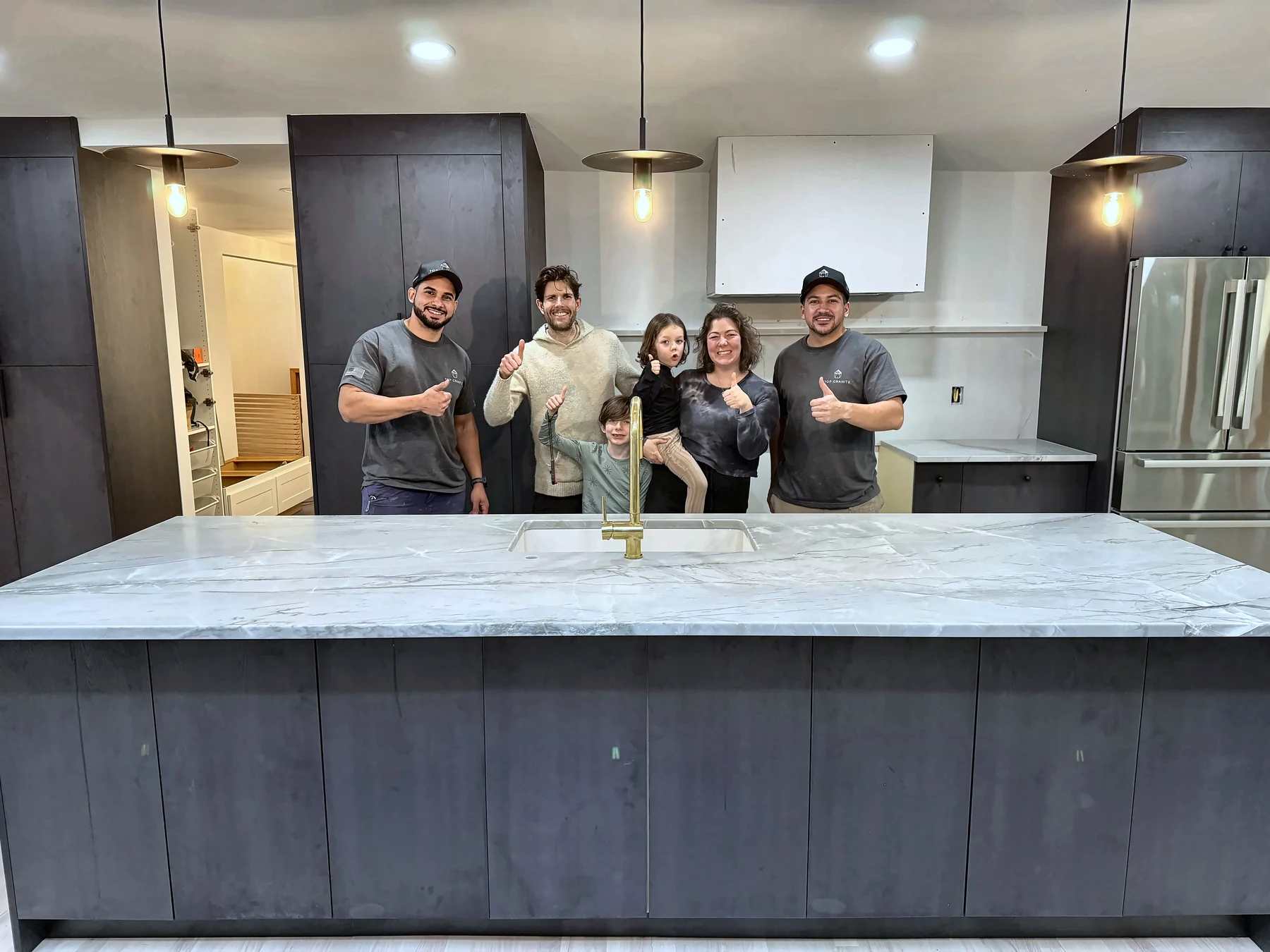 Top Granite team giving a thumbs-up with a client family in their finished kitchen