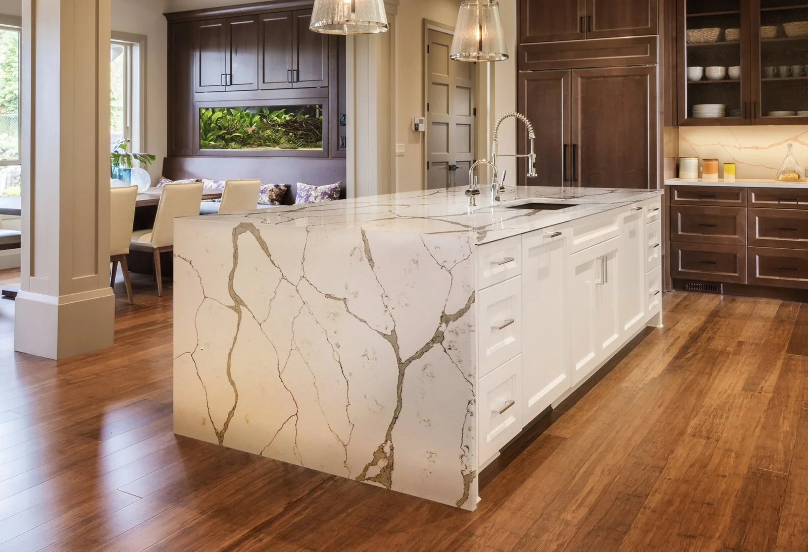 White waterfall island with bold gray veining, dark cabinets, and wood flooring