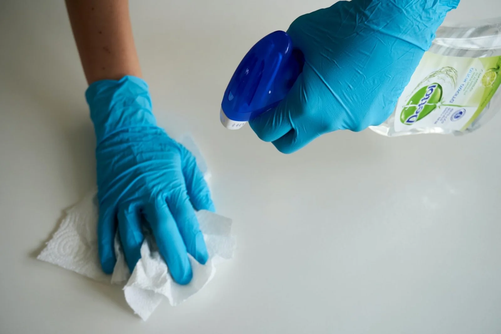 Gloved hands wiping a light countertop beside a spray bottle
