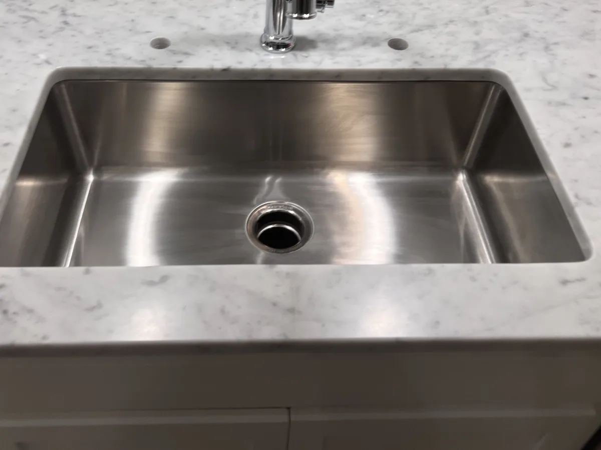 Large single bowl stainless undermount sink set into a white marble countertop