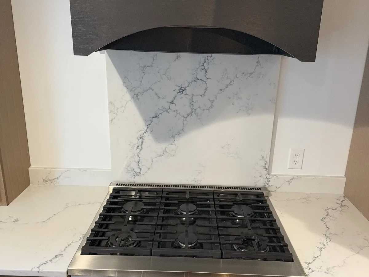 Gas range set between narrow bands of white veined quartz countertop with a matching stone backsplash