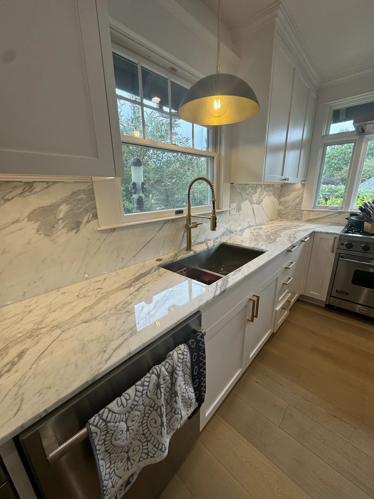 Marble kitchen counter with a full height marble backsplash, a workstation sink, a gold faucet and a professional range