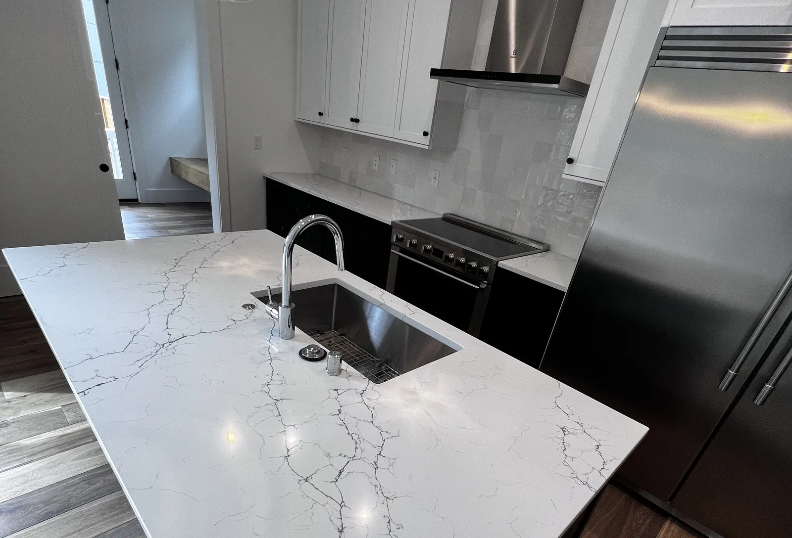Kitchen island in white veined quartz with an undermount sink and chrome faucet, white cabinets, a stainless range and a tile backsplash behind