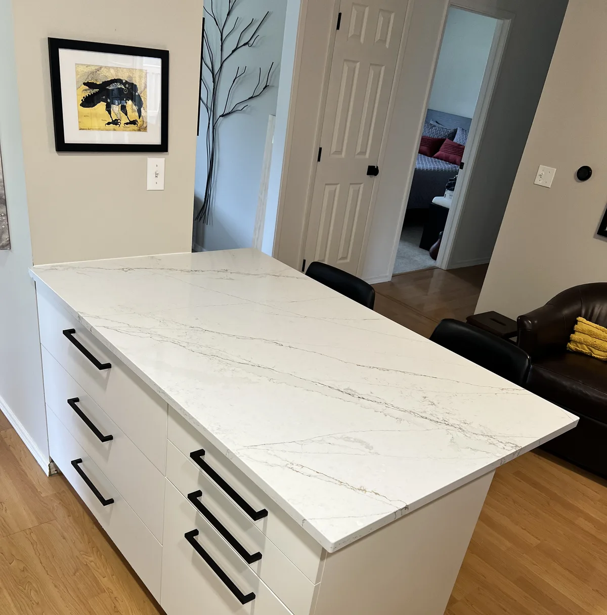 Kitchen island in white veined stone with white cabinet fronts and black bar pulls, in a furnished open plan home
