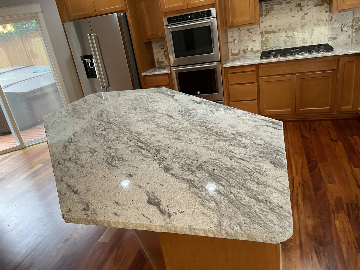 Granite kitchen island with a shaped edge in a kitchen with wood cabinets