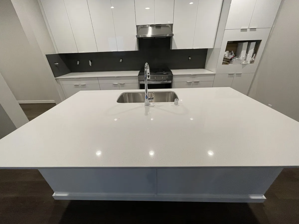 Large white quartz kitchen island with an undermount sink in a modern white kitchen