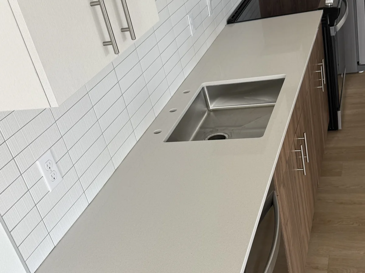 Long straight quartz countertop run passing an undermount sink, a dishwasher and a cooktop