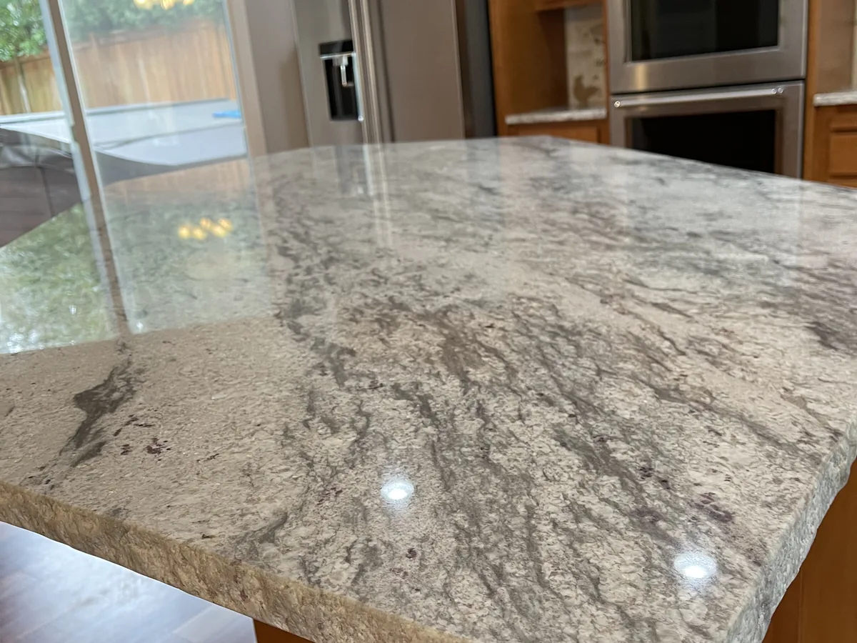 Granite island with a rough chiseled edge and a rounded corner in a wood cabinet kitchen