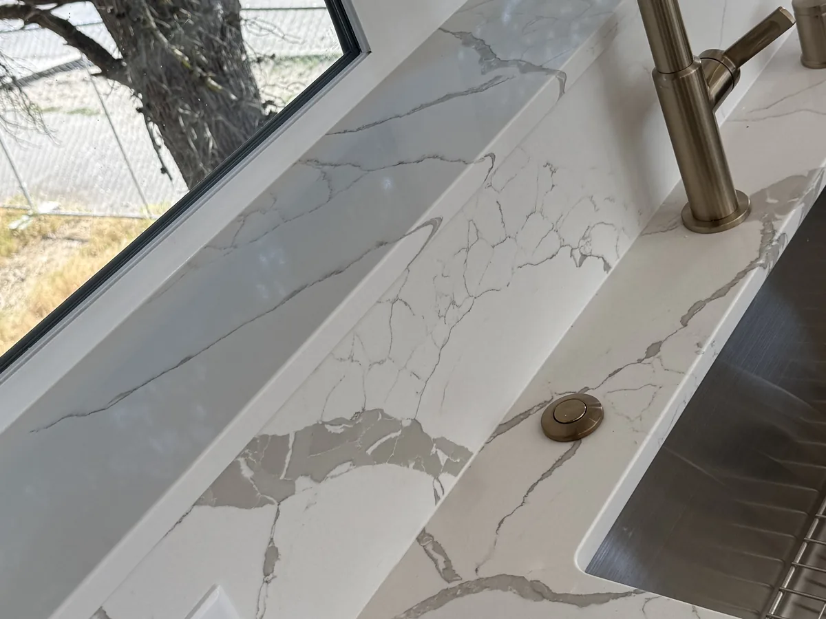 Veined quartz countertop and matching backsplash beside an undermount sink, with fine grey lines running through the stone
