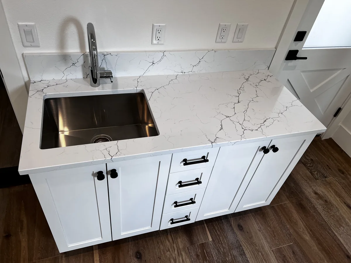 White veined quartz counter with an undermount stainless sink, a quartz backsplash and white shaker cabinets