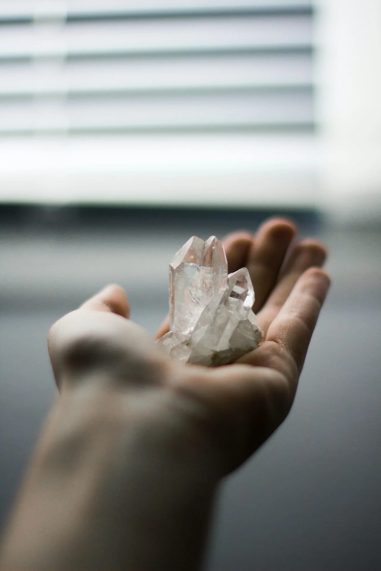 Hand holding a clear quartz crystal in soft window light