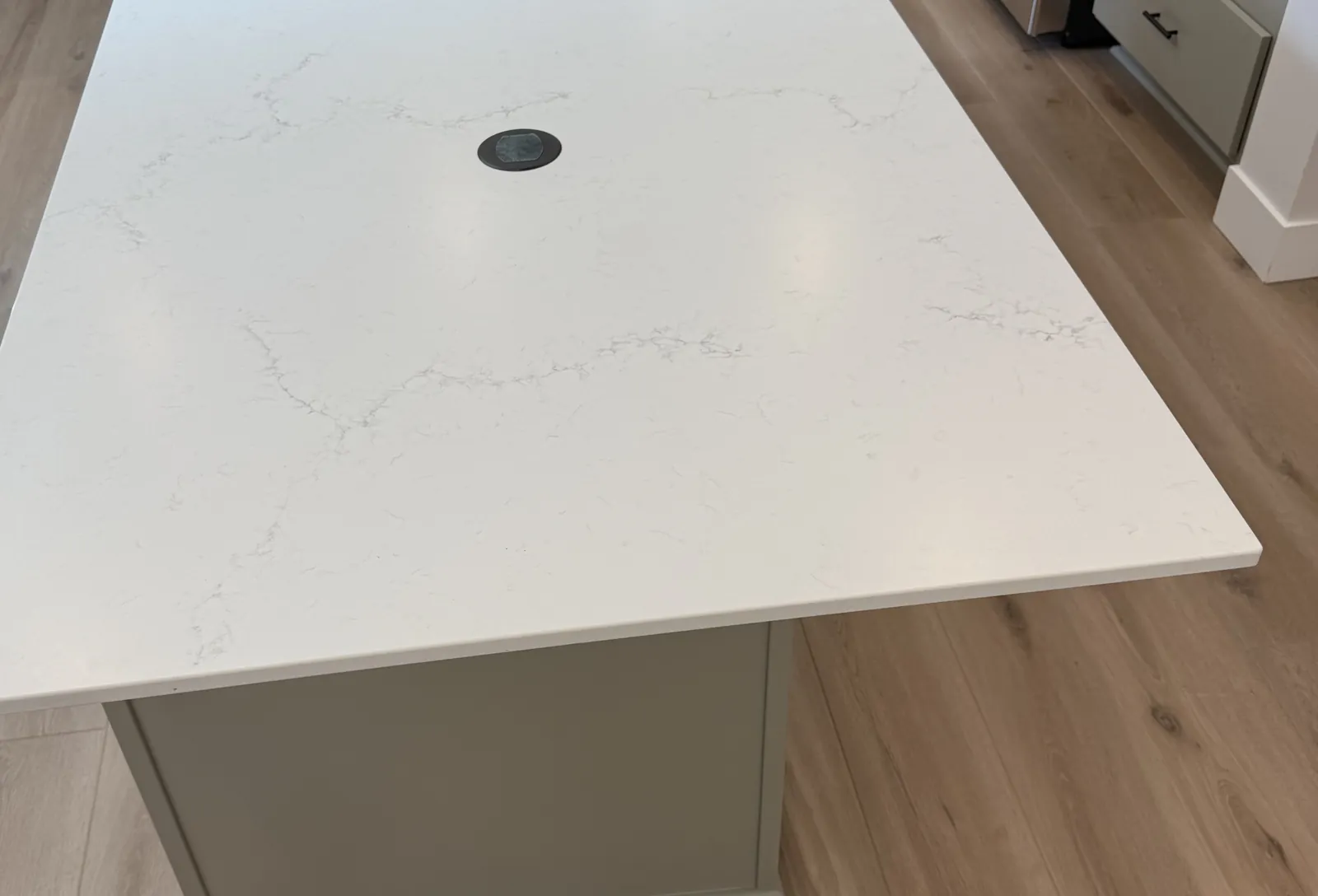 Kitchen island with a white quartz top overhanging a painted base cabinet above a wood floor