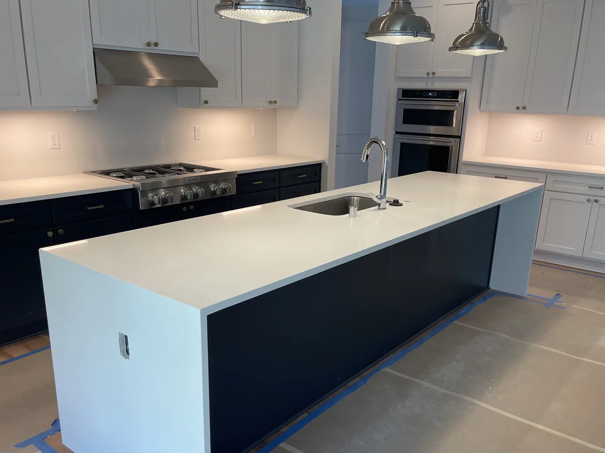Long kitchen island with a white quartz top reaching past the dark base cabinet, leaving a visible overhang