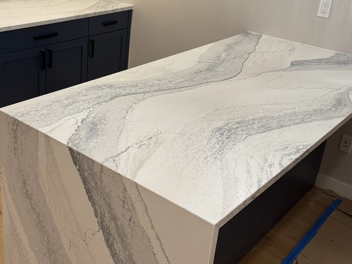 Island with a mitred waterfall edge in veined quartz, the top projecting past the dark cabinet base