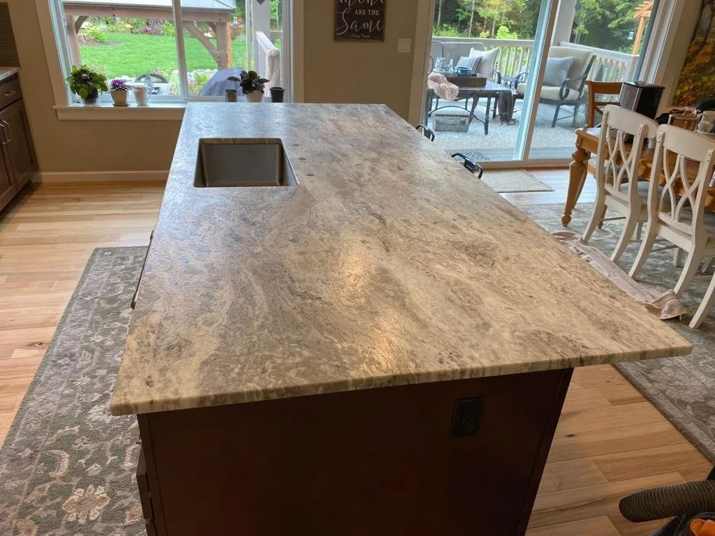 Broad stone island with a sink beside a dining area and windows