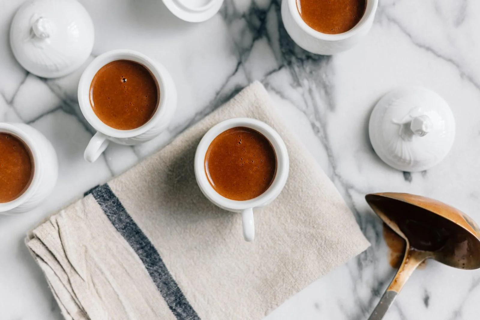Cups of tea and a white teapot on a pale veined surface