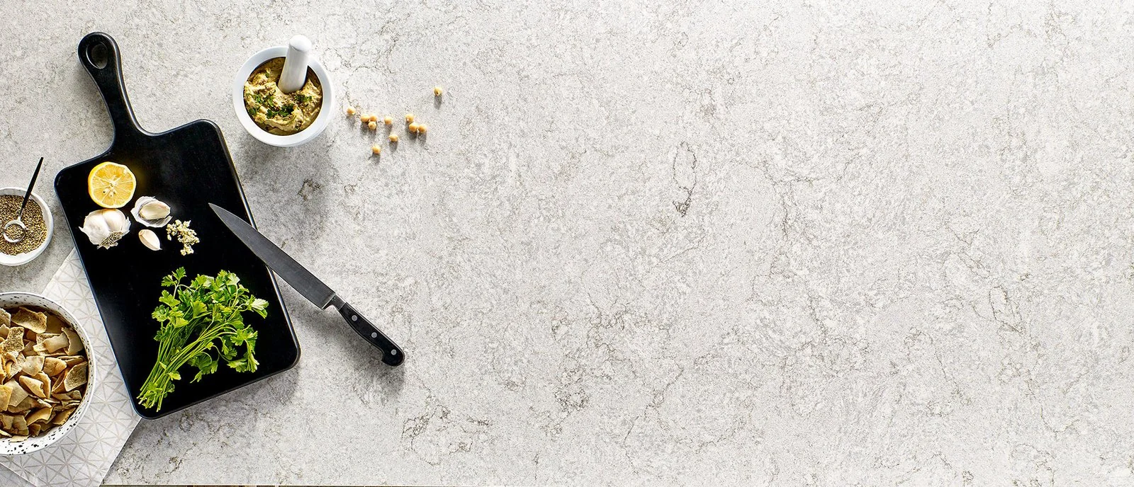 Overhead view of a pale patterned counter with vegetables and a black cutting board