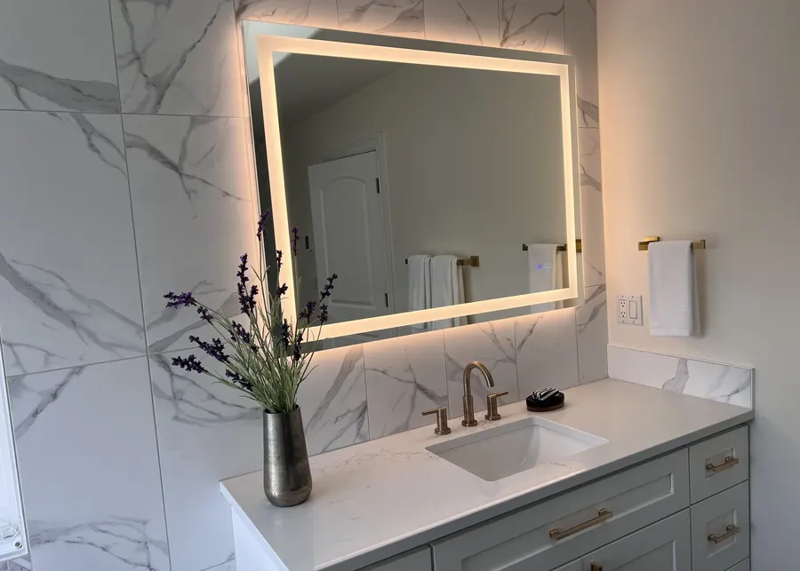 Bathroom vanity with a marble wall and lit mirror. A Top Granite project