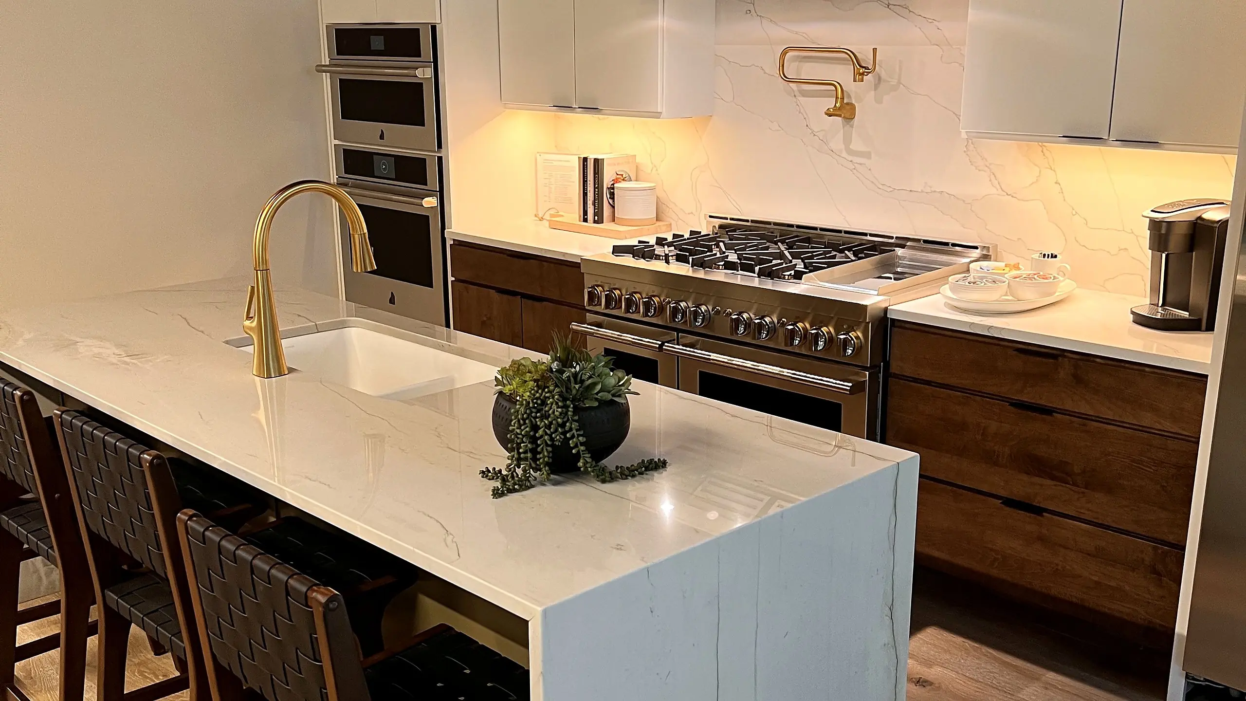 White quartz waterfall island with a brass faucet, walnut cabinets and a professional range in a bright kitchen