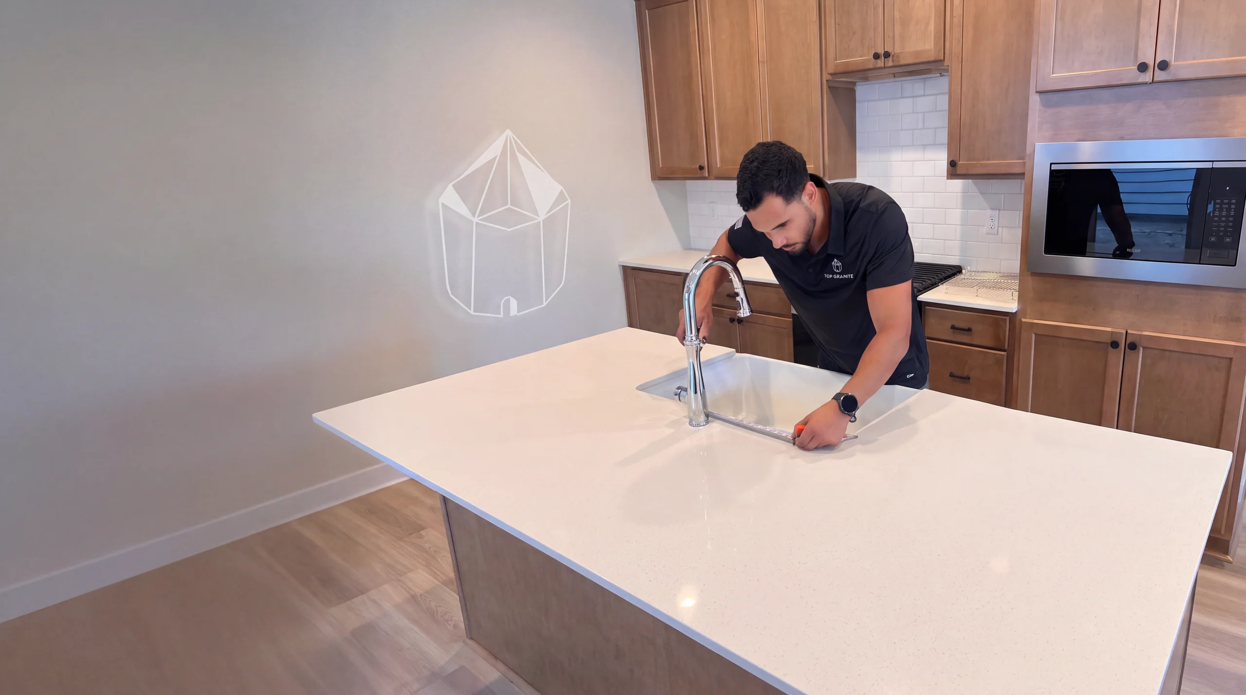 Johnny of Top Granite measuring a sink cutout on a white quartz island, with the Top Granite symbol on the wall
