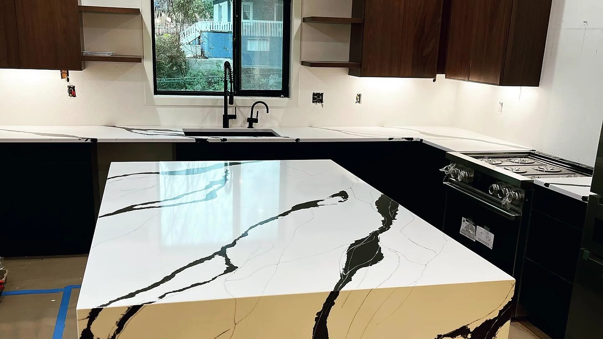 White quartz island with bold dark veining installed by Top Granite in a black-cabinet kitchen