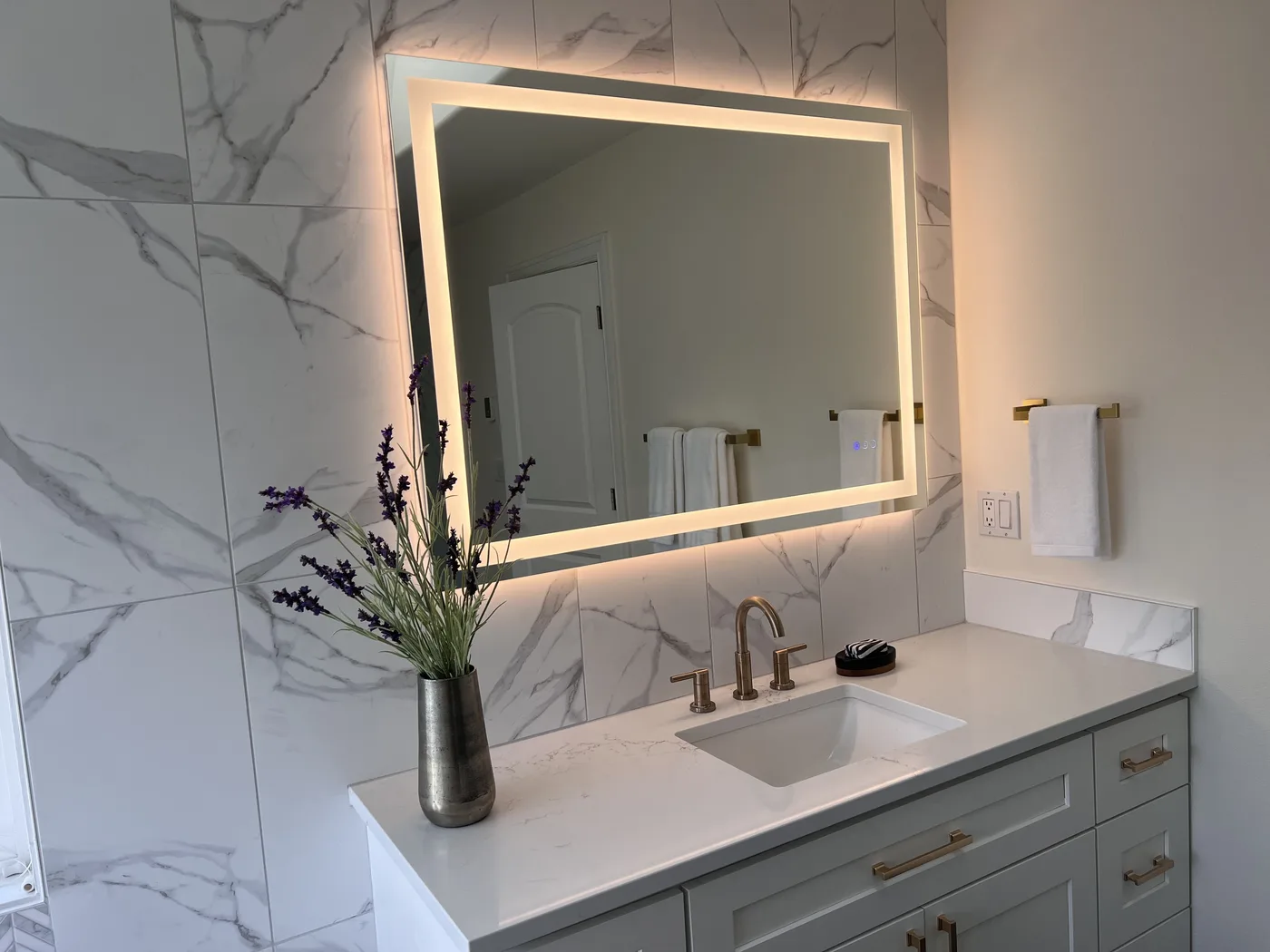 Bathroom vanity with a marble wall and lit mirror. A Top Granite project